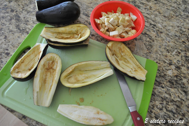 A green cutting board with eggplants sliced in halves and hollowed out and chopped inside a red bowl.
