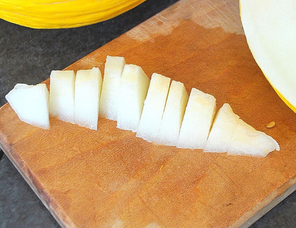 On a cutting board, sliced a yellow melon into small pieces.