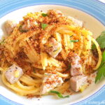 A blue and white dish with a serving of spaghetti with cubes of fresh tuna, topped with crispy bread crumbs.