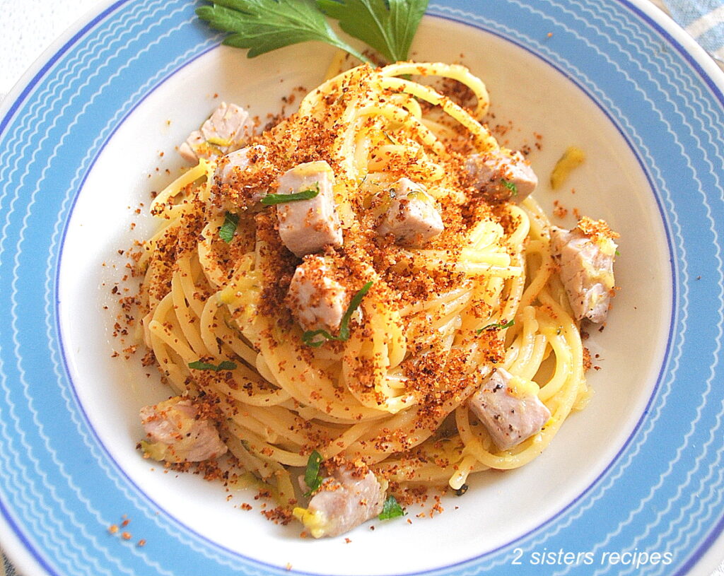 A blue and white dish with a serving of spaghetti with fresh tuna topped with crispy bread crumbs.