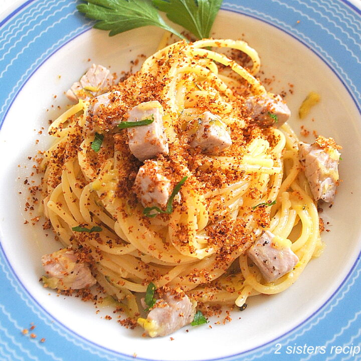 A blue and white dish with a serving of spaghetti with fresh tuna topped with crispy bread crumbs.