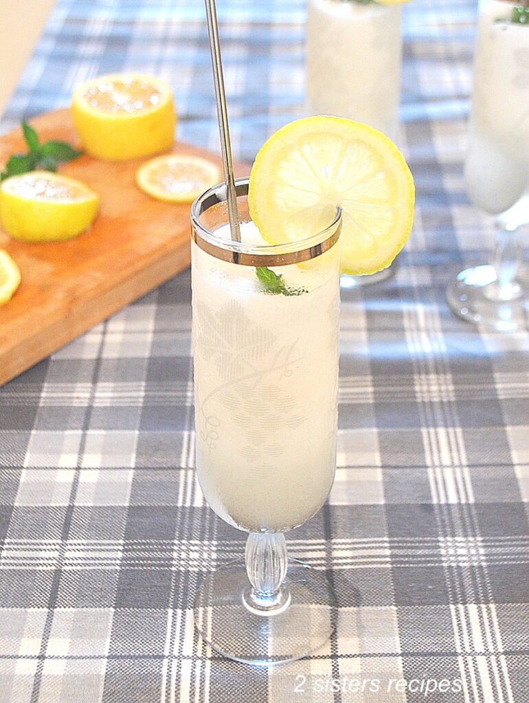 A tall fluted glass filled with a white sorbet, topped with a lemon slice and mint leaf, with a wood cutting board with slices of lemon next to it.