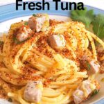 A blue and white plate with spaghetti topped with toasted bread crumbs and cubes of ahi tuna.