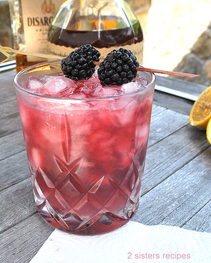 A crystal cocktail glass filled with blackberry smash cocktail drink with 2 fresh blackberries on a pick as a garnish.