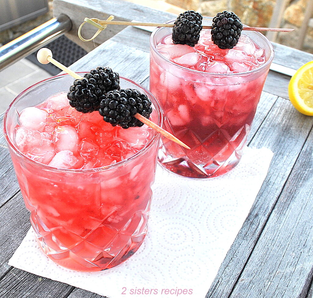 2 glasses filled with purple-tint cocktail, and crushed ice with 2 blackberries on a pick.