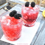 2 glasses filled with light purple color drink over crushed ice, and with 2 blackberries on a pick.