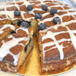 A cake topped drizzled glaze, and fresh blueberries inside an out.