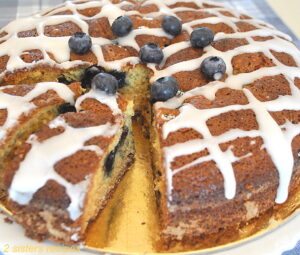 A cake topped drizzled glaze, and fresh blueberries inside an out.