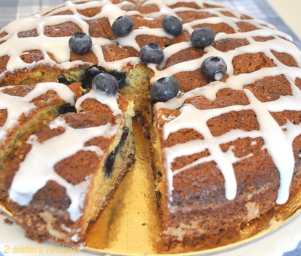 A cake topped drizzled glaze, and fresh blueberries inside an out.