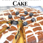 A cake topped drizzled glaze, and fresh blueberries inside an out.