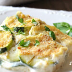 A white plate with a serving of creamy potato and zucchini au gratin.
