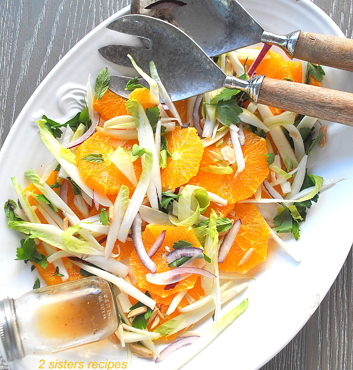 A white oval platter filled with sliced oranges, endives, red onions and tossed with fresh heabs.