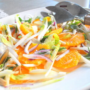 A white platter filled with sliced oranges, endives, red onions and fresh herbs.