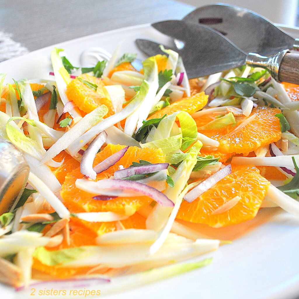 A fall salad served on a white platter filled with sliced Navel oranges, endives, red onion and toasted almonds/