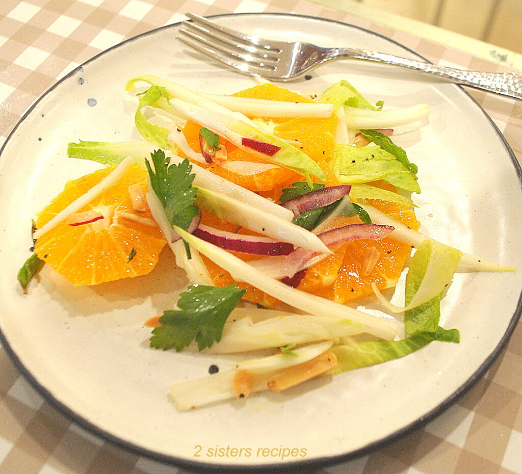 A salad plate with a serving of an orange endive salad and a fork on the side.