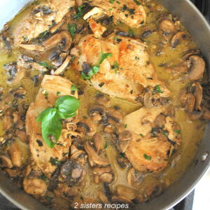 A large skillet filled with pieces of chicken, sauce and fresh parsley scattered on top.