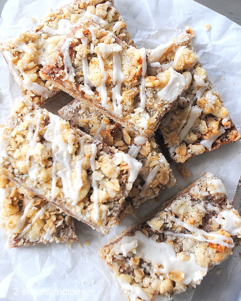 A few of the apple crisp bars with icing drizzled on top piled on a sheet of parchment paper.