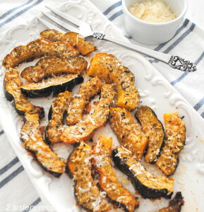 A white rectangular platter filled with baked parmesan-crusted acorn slices.