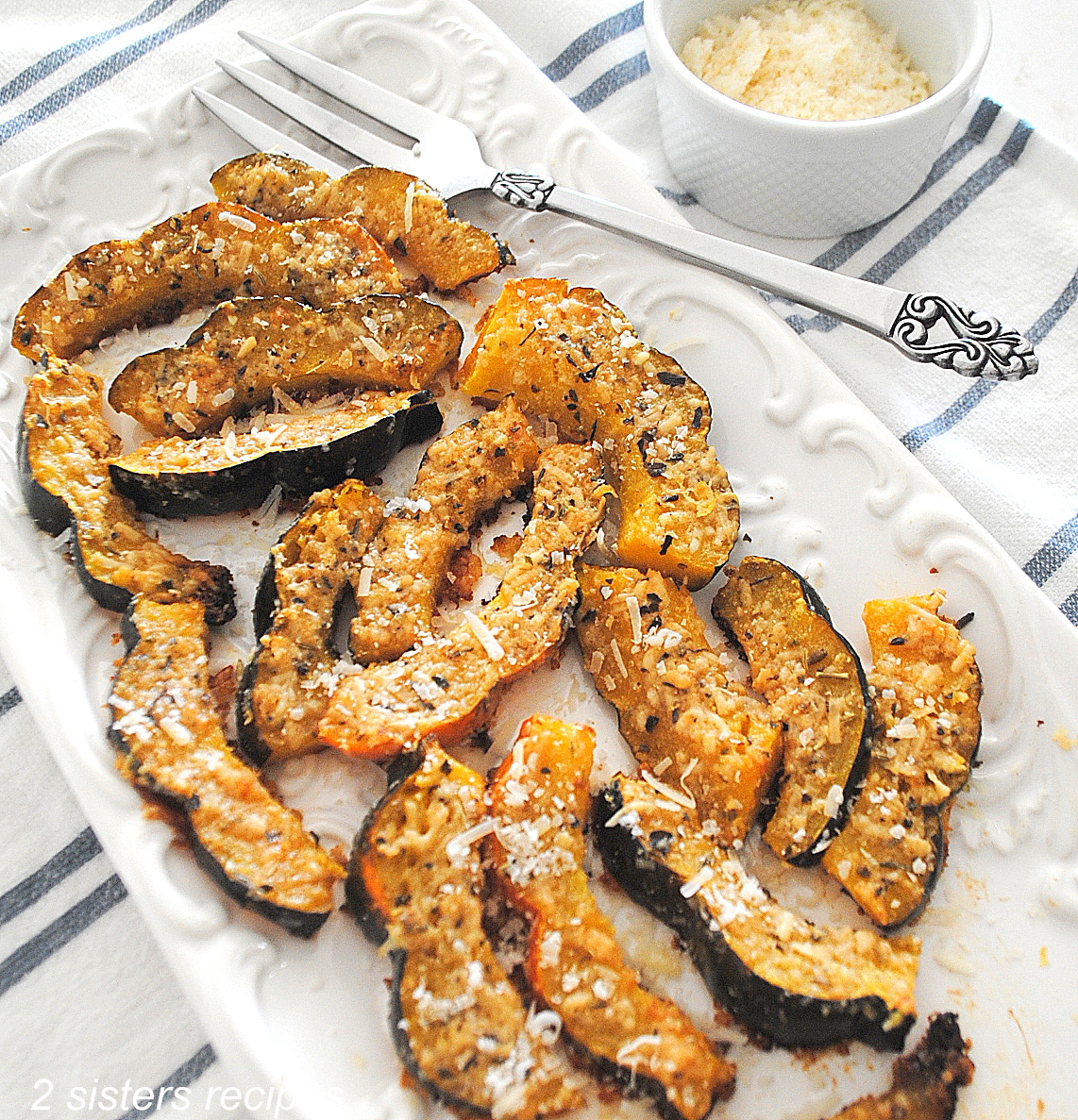 A white rectangular platter filled with baked parmesan-crusted acorn slices.