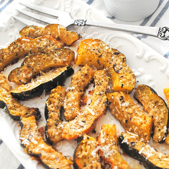 White platter filled with slices of baked acorn squash topped with parmesan-herb crust.