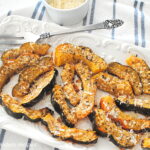 A white platter filled with slices of acorn squash baked with parmesan coating.