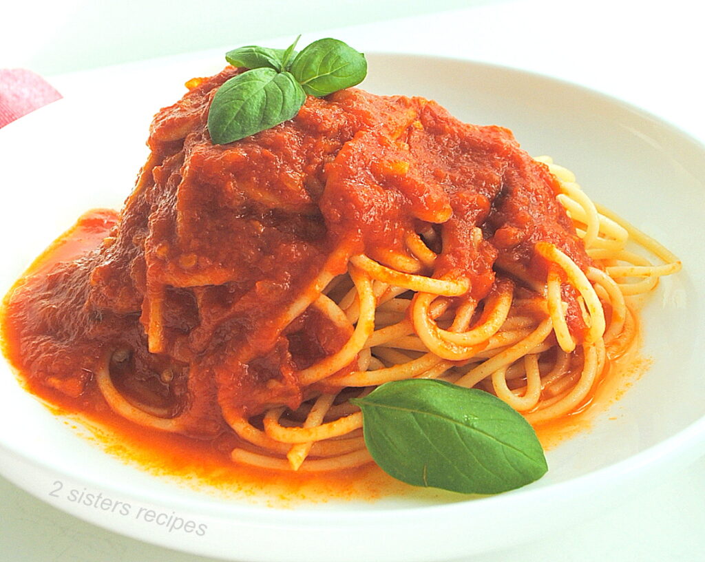 A white bowl filled with cooked spaghetti with tomato sauce and fresh basil leaves on top.