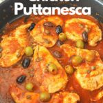 A black skillet filled with cooked chicken breasts in a puttanesca sauce.