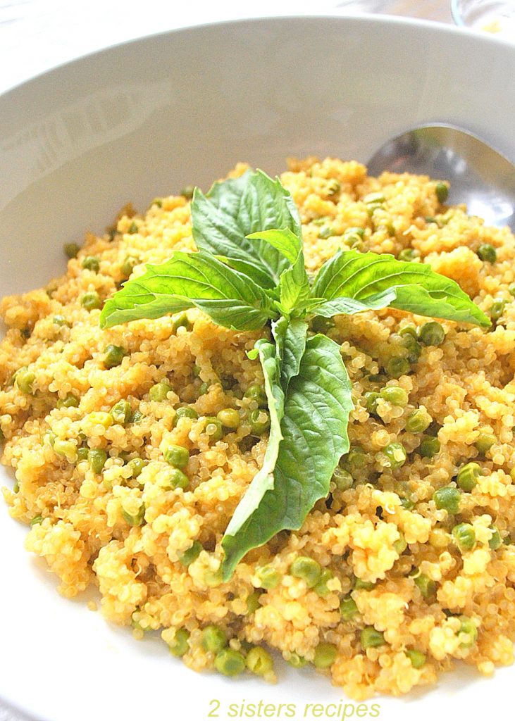 A white bowl filled with baby peas and cooked quinoa with fresh basil leaves on top.