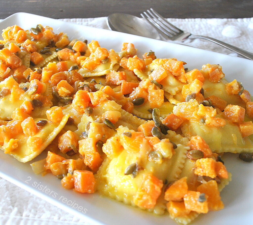 A large white platter filled with cooked ravioli topped with chopped butternut squash and toasted pepitas.