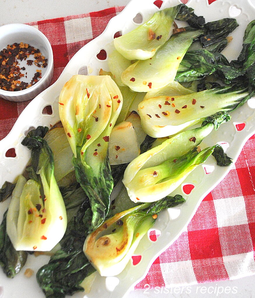 A white oval platter filled with sautéed bok choy with red pepper flakes scattered on top.