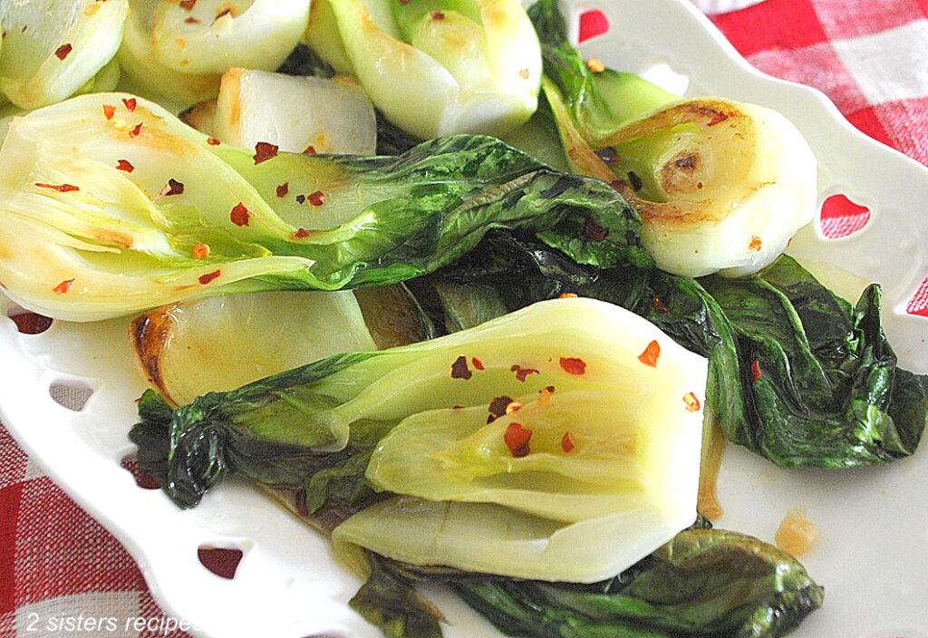 A white platter filled with sautéed bok choy with red pepper flakes scattered on top.
