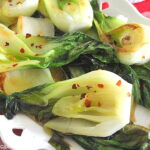 A white platter filled with sautéed bok choy with red pepper flakes scattered on top.