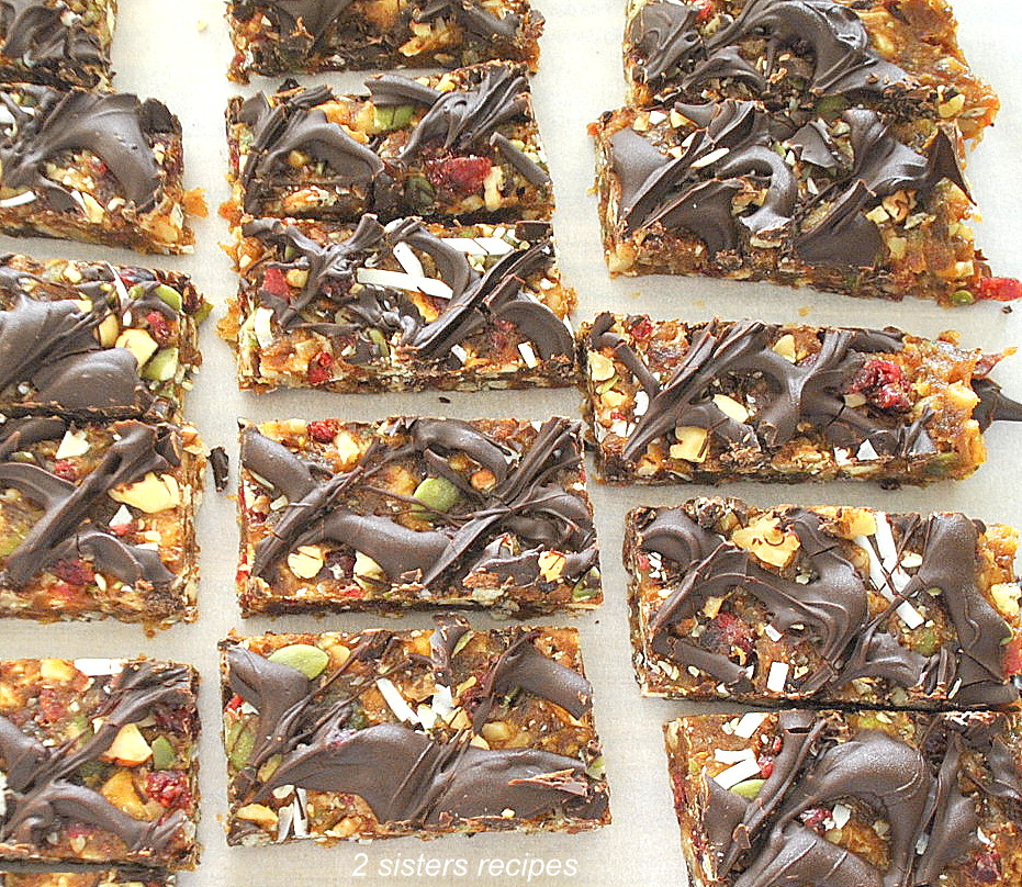 On sheet of parchment paper are fruit & nut protein bars with chocolate drizzled on top.