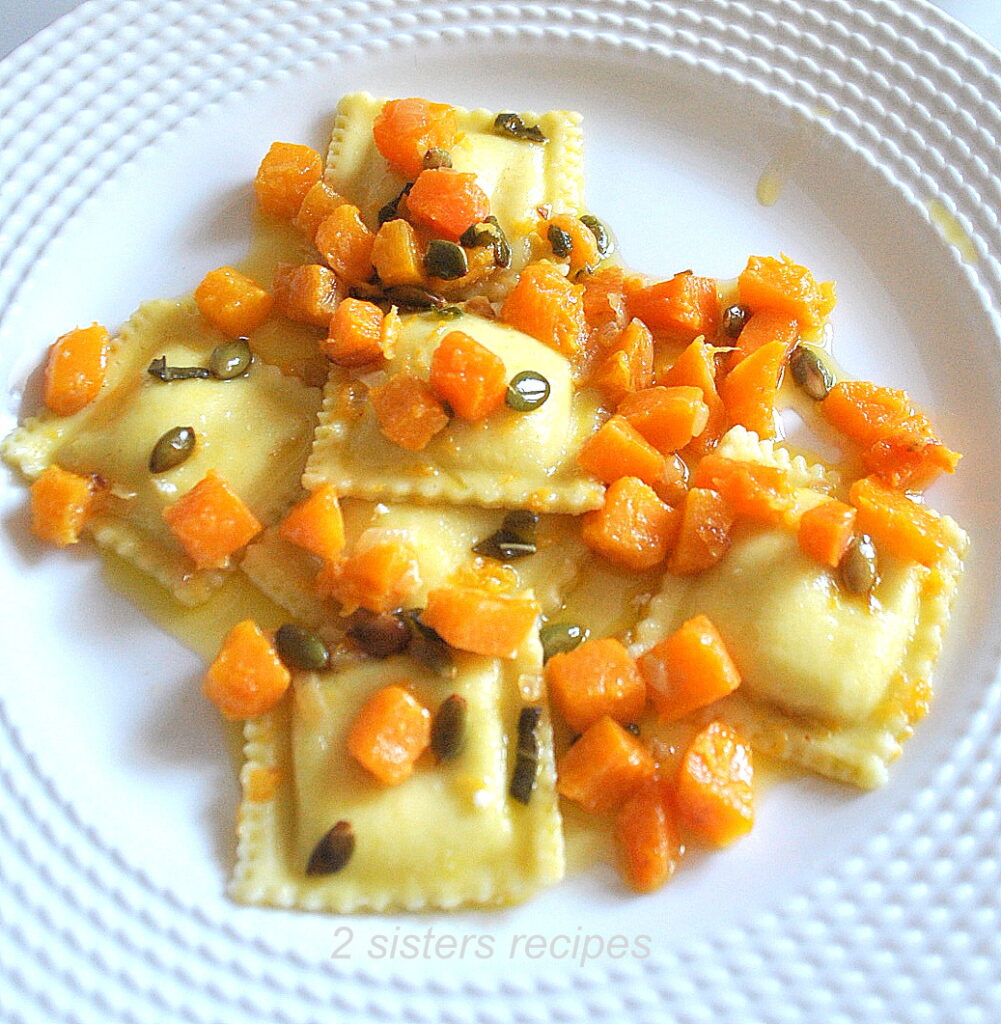 A white plate filled with ravioli topped with chunks of butternut squash and toasted pepitas.