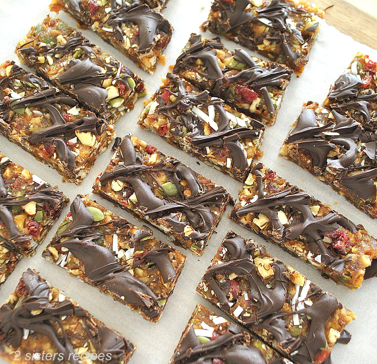 On white parchment paper are fruit & nut protein bars with chocolate drizzled on top.