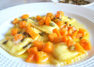 A white dinner plate filled with ravioli topped with chunks of butternut squash and toasted pepitas in a butter sauce.