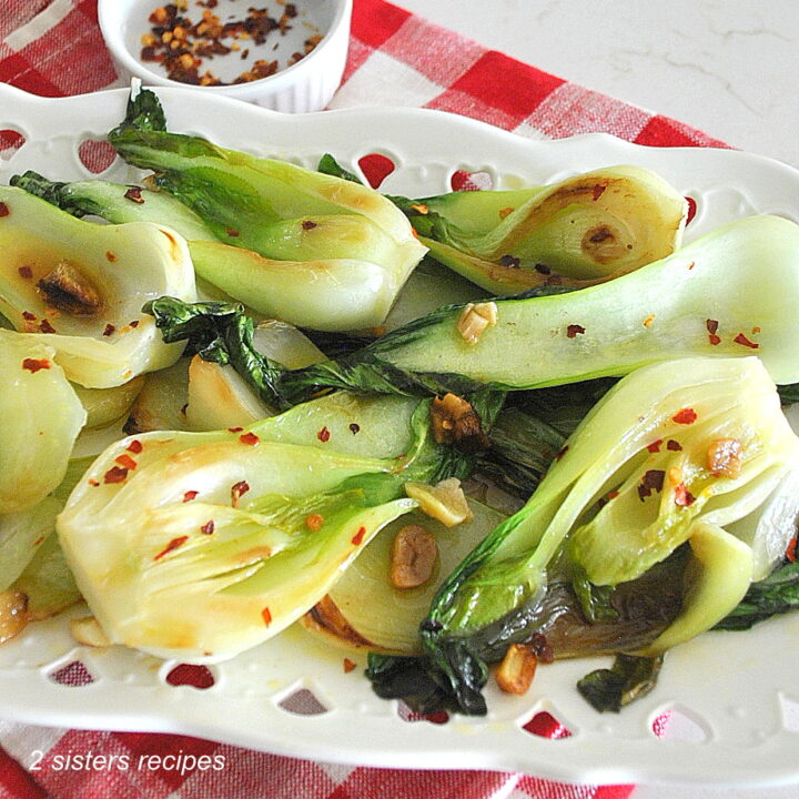 Sauteed bok choy served on a white platter with red pepper flakes scattered on top.