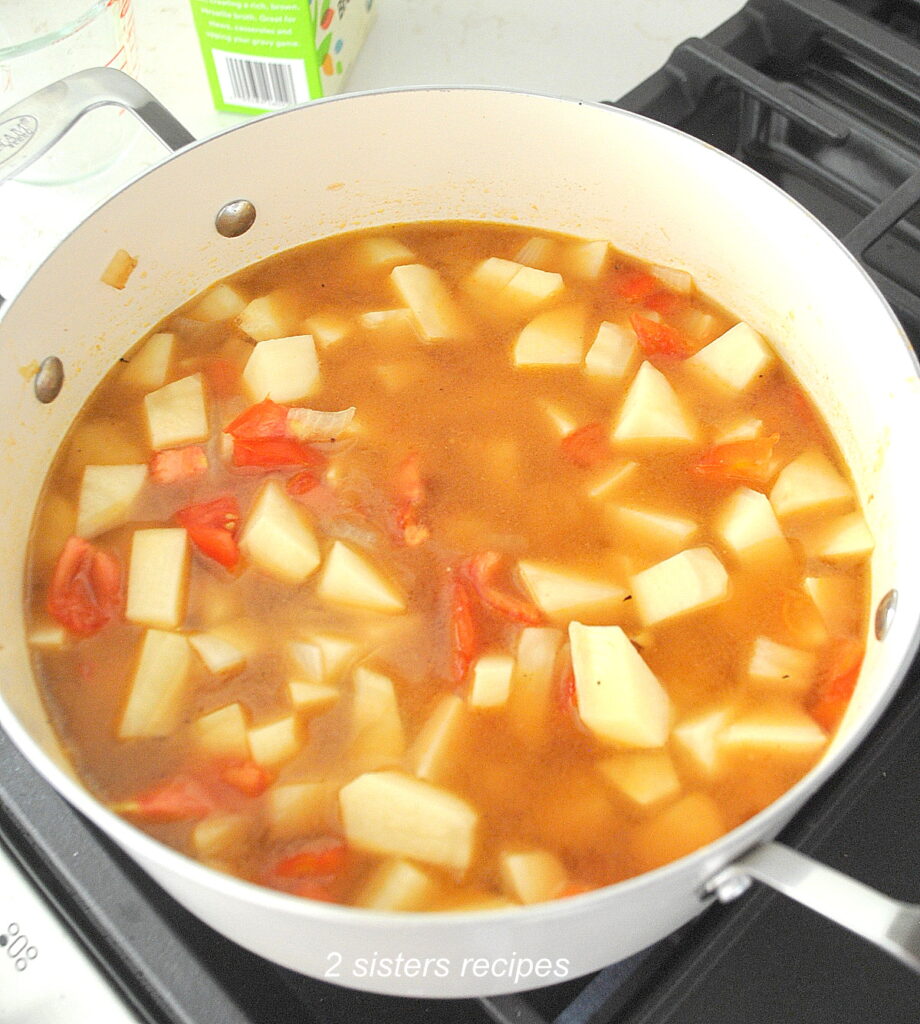 A large Dutch oven pot filled with chopped potatoes, tomato and vegetable broth.