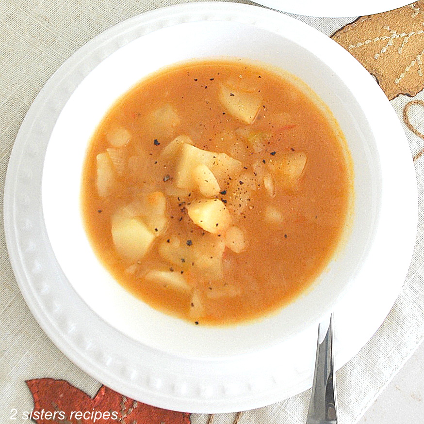 A white bowl and plate with a spoon on the side, filled with a thick potato soup.