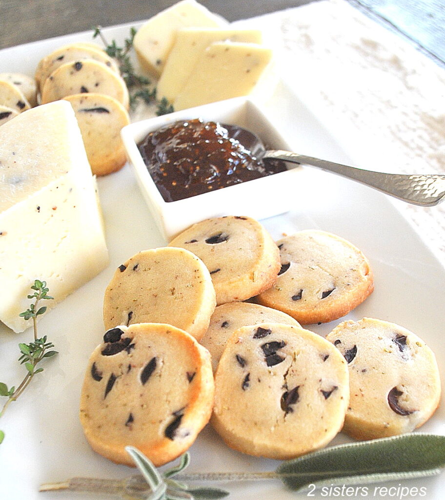 A white plate with shortbread biscuits, a wedge of cheese, and some jam next to them.