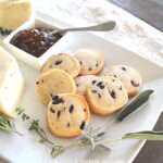 A white platter filled with shortbread biscuits studded with black olives, served with fig jam as an appetizer.