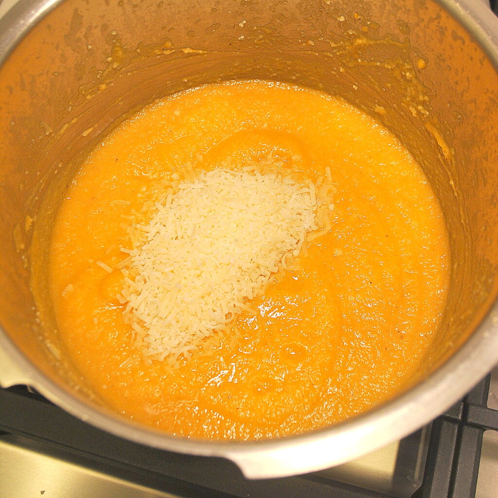 A large pot filled with sweet potato soup with grated parmesan cheese tossed on top.