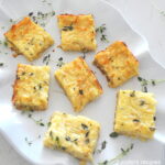 A large white platter filled with baked eggs and onions squares with sprigs of fresh thyme around them.