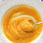 A spoonful of creamy sweet potato cauliflower soup served in a white bowl.