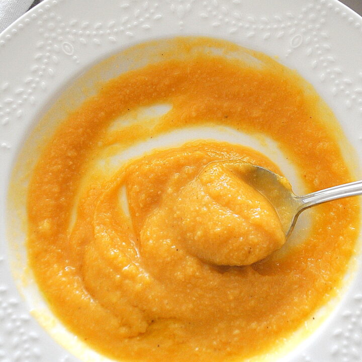 A spoonful of creamy sweet potato cauliflower soup served in a white bowl.