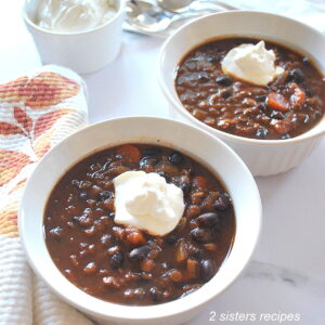 Two white bowls filled with lentil and black bean chili with a dollop of sour cream on top.
