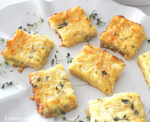 A white platter filled with onion, cheese and egg baked squares with fresh thyme as garnish.