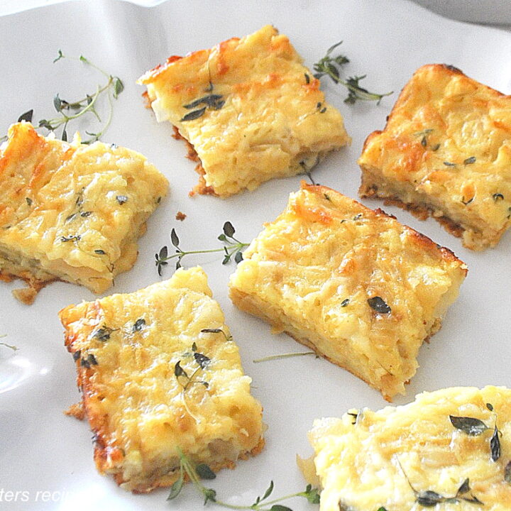 A white platter filled with onion, cheese and egg baked squares with fresh thyme as garnish.