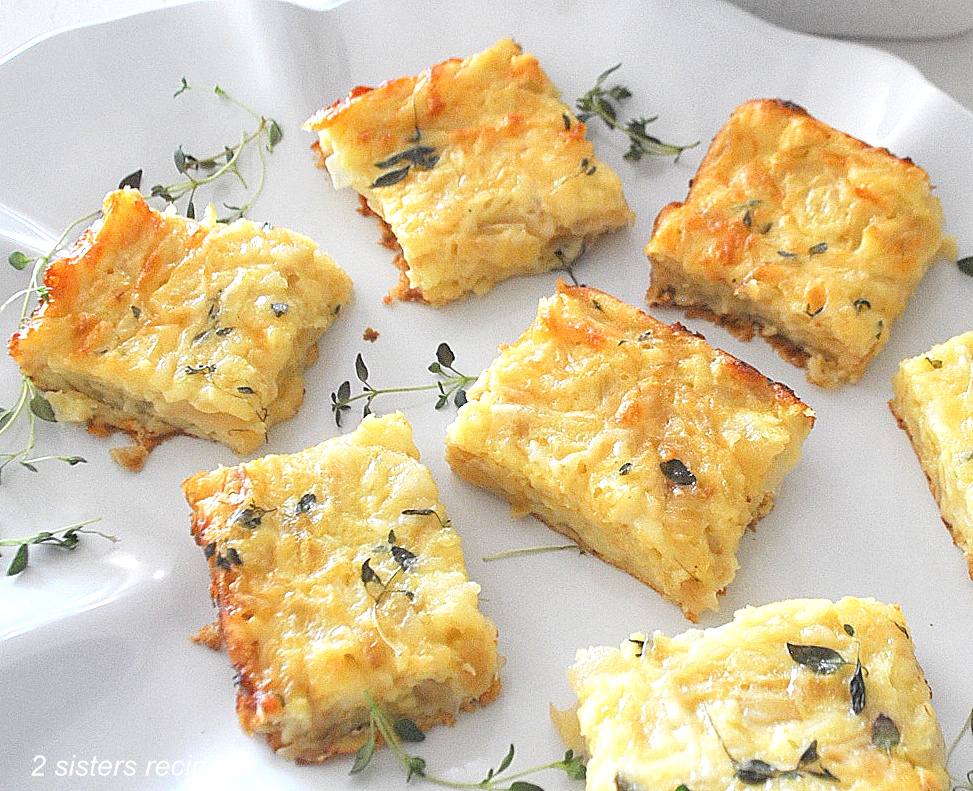 A white platter filled with onion, cheese and egg baked squares with fresh thyme as garnish.