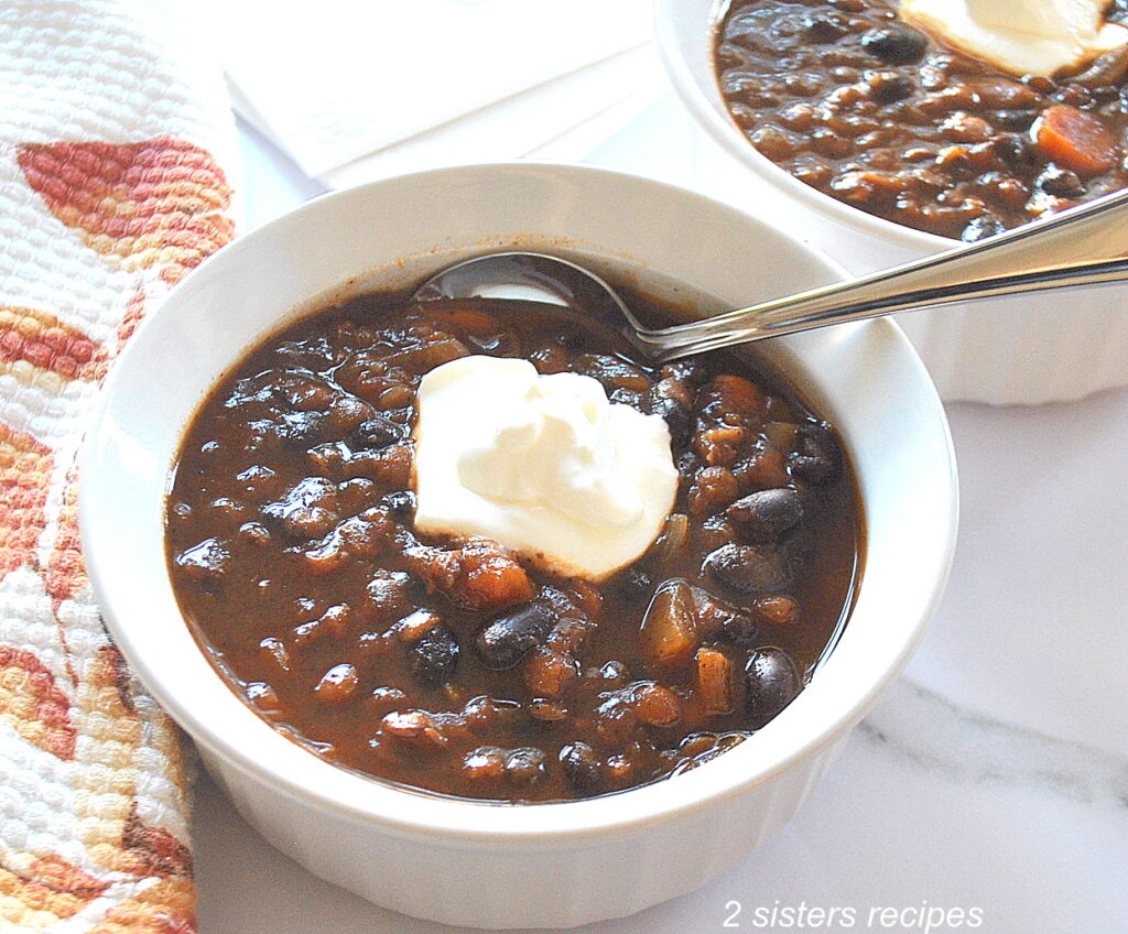 A white bowl filled with chili with a spoon inside and a dollop of cream on top.
